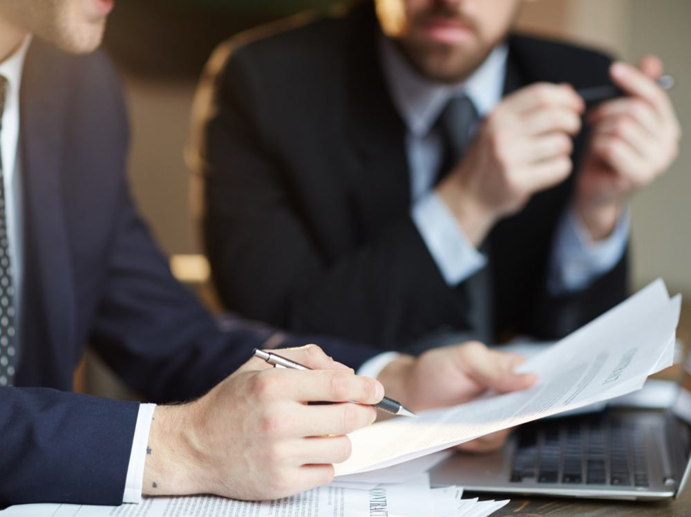 Successful Business Partners Discussing Contract Closeup portrait of two unrecognizable business partners reviewing paperwork and signing contract papers at table during meeting